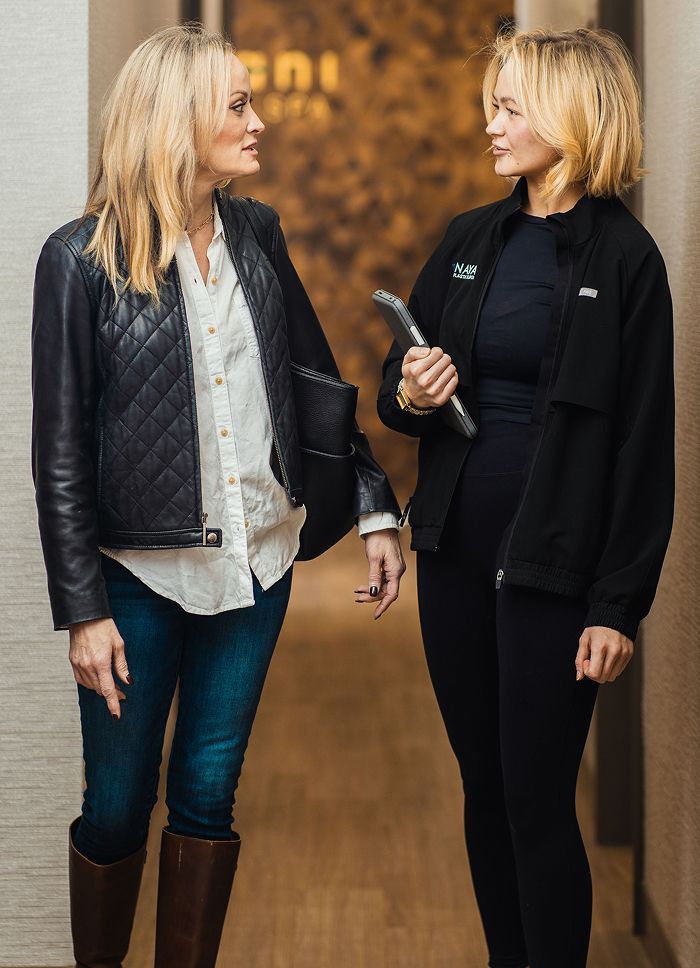 Two women in casual conversation inside a hallway.