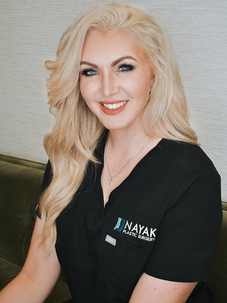 Smiling woman in medical scrubs, plastic surgery office.