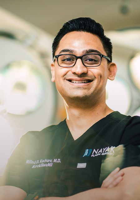 Doctor in scrubs smiling confidently indoors.