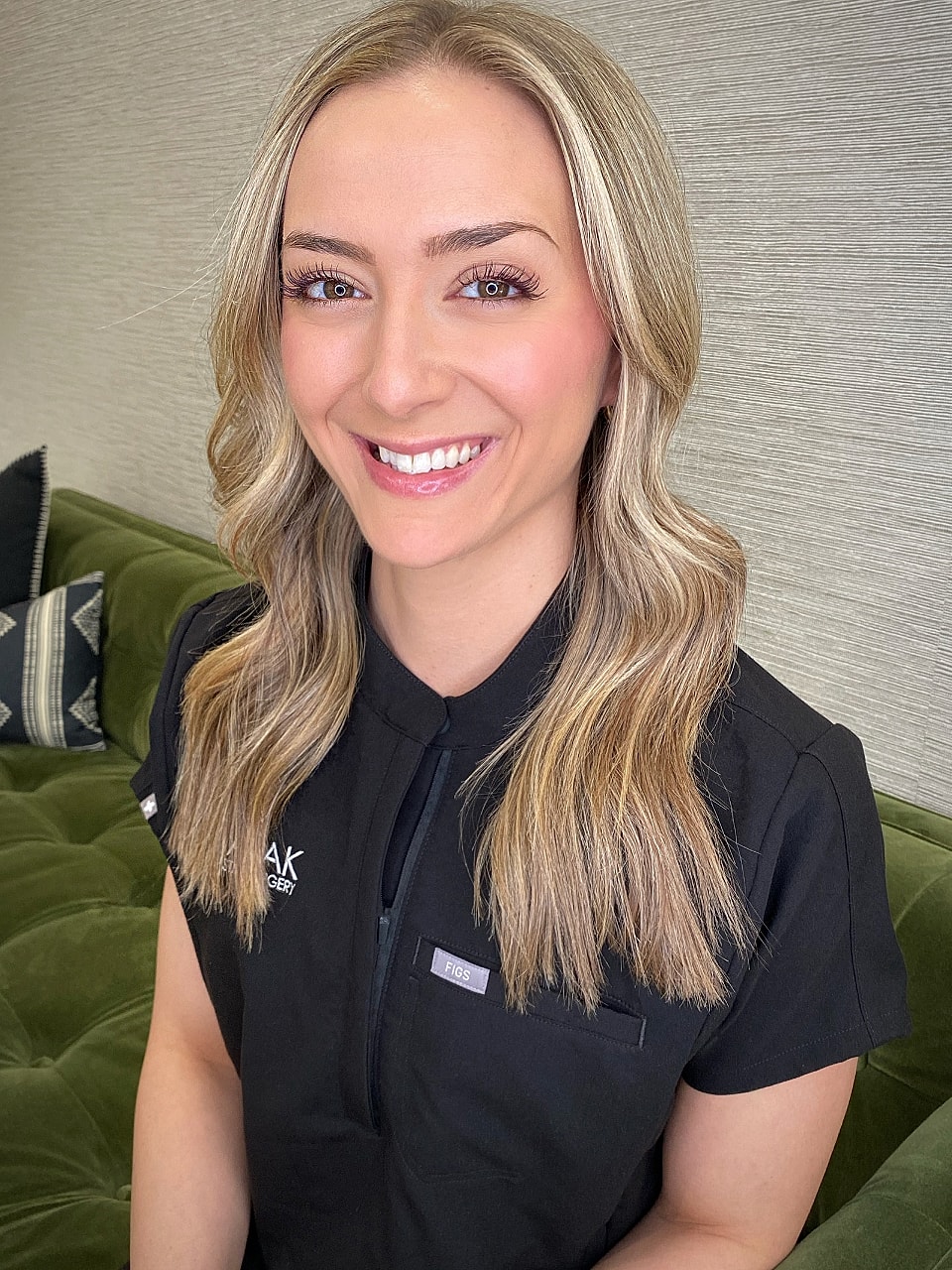Smiling professional in black attire, green background.