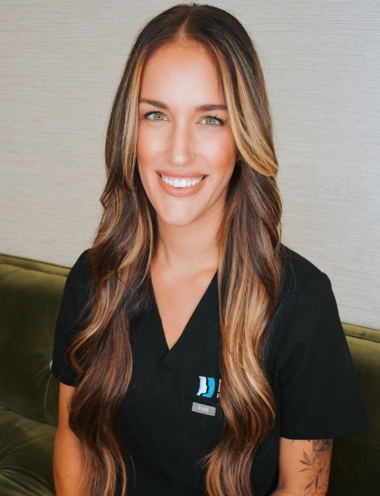 Smiling woman in medical scrubs, sitting indoors.