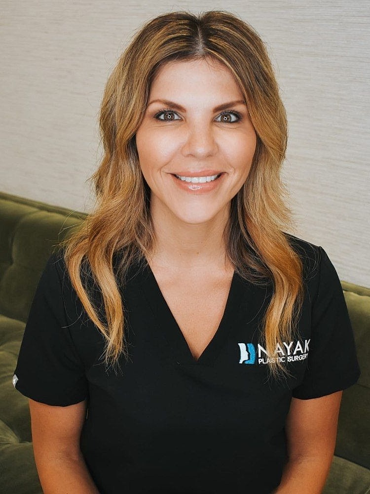 Smiling woman in medical attire, plastic surgery setting.
