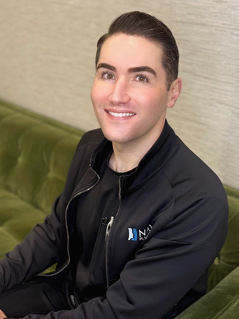 Smiling man in black jacket on green sofa.