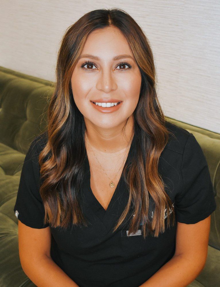Woman in scrubs smiling on green couch.