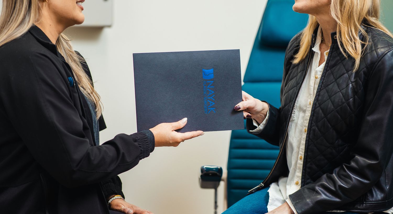 Two women exchanging documents in an office setting.